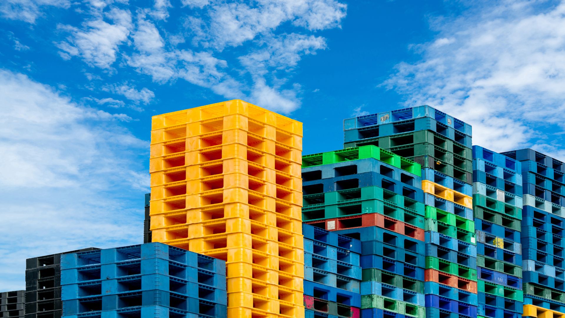 Colorful plastic pallets stacked high against a bright blue sky.