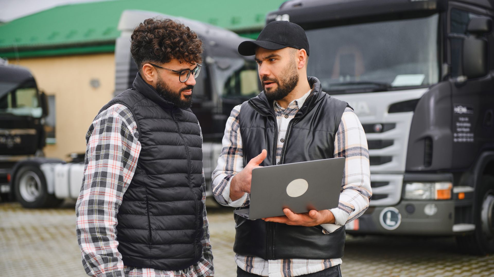 Two fleet managers stand outside discussing data in front of a tablet.