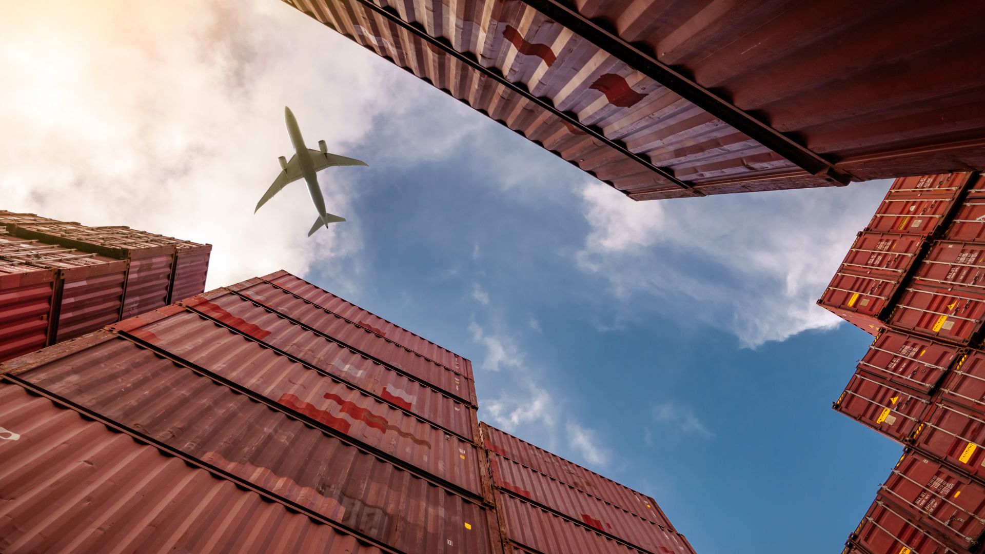 Large shipments shot low under a blue sky and an aeroplane.